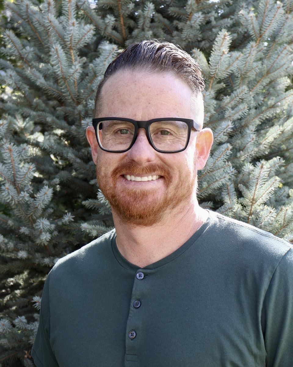 Kevin Barr smiling in a green henley in front of evergreen trees